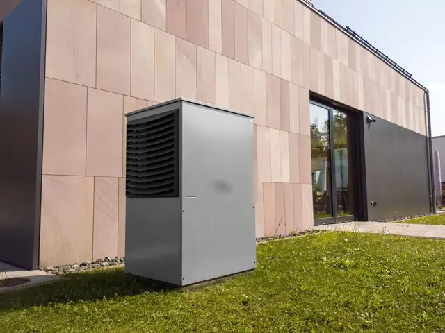 Modern heat pump outdoor unit on a lawn beside a house wall